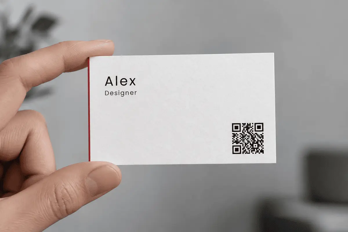 A minimalist business card held between two fingers, with a small QR Code printed in the lower right corner
